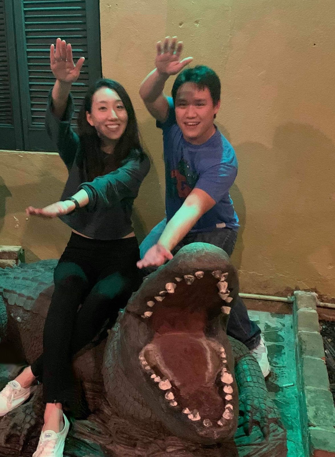 Elaine and Lawrence striking a pose on a giant alligator statue in a courtyard at night